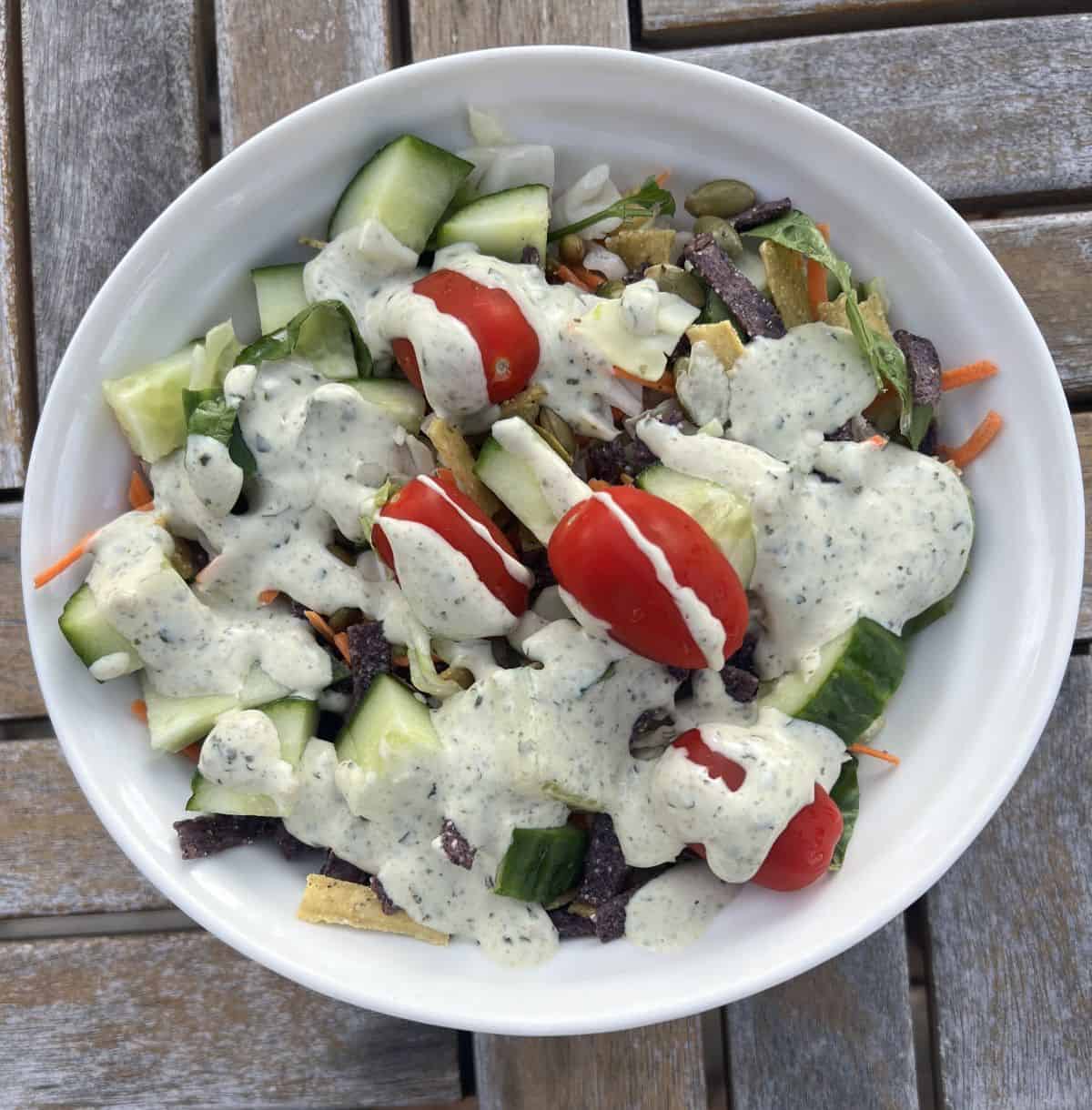 Top down image of the salad kit served in a white bowl with dressing and toppings on it. 
