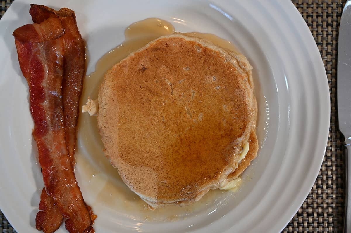 Top down closeup image of a white plate with two pancakes on it and two strips of bacon.