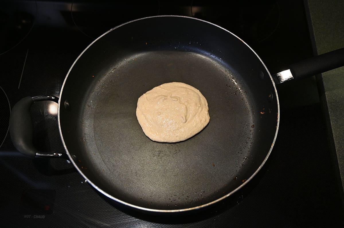 Image of raw pancake batter being cooked in a frying pan on the oven.