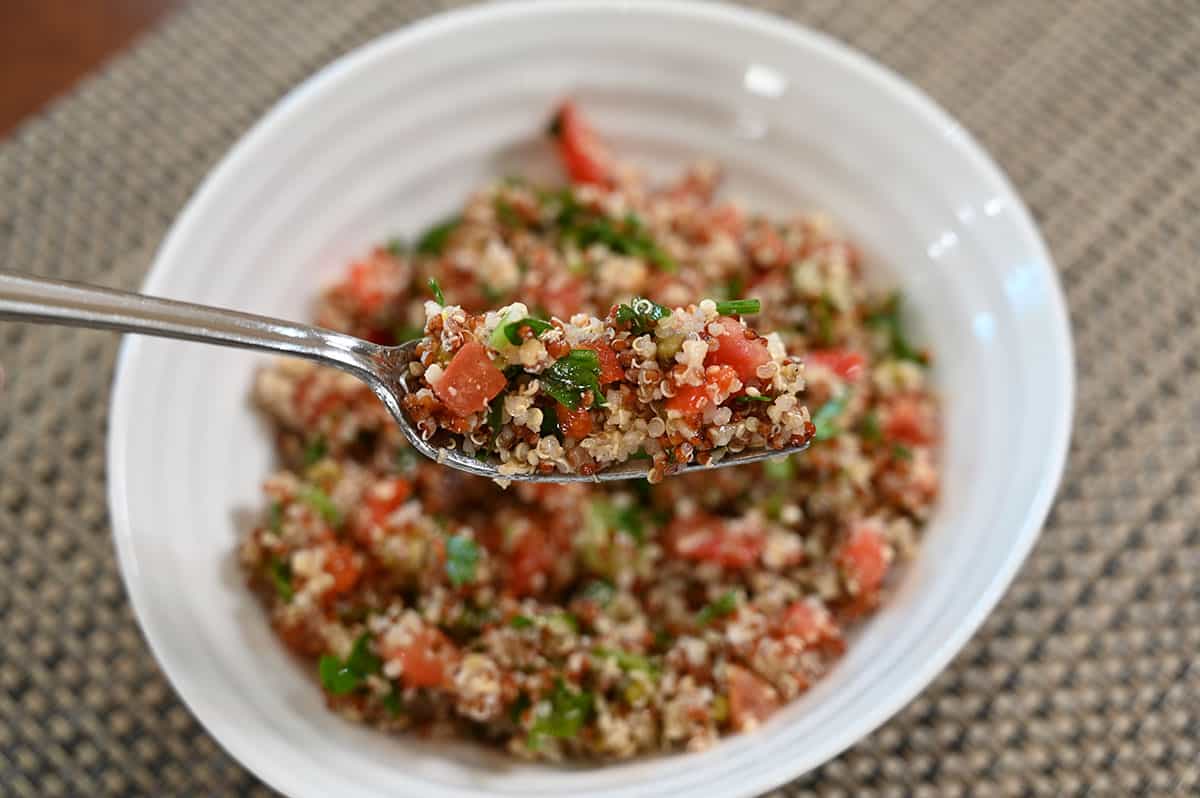 Closeup image of a forkful of the Costco Kirkland Quinoa Salad with a bowl of quinoa salad in the background.