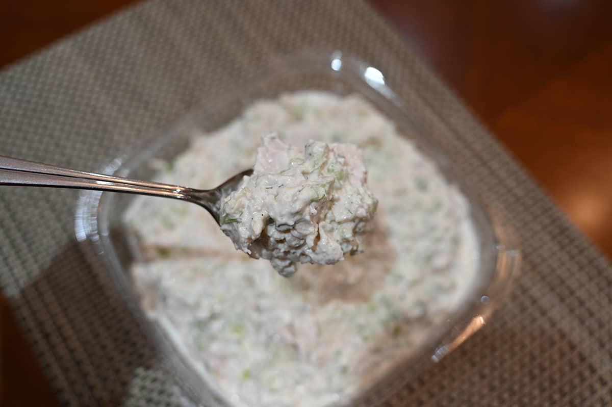 Image of an open container of the Costco Kirkland Signature Chicken Salad from Costco with a spoon taking some out of the container.