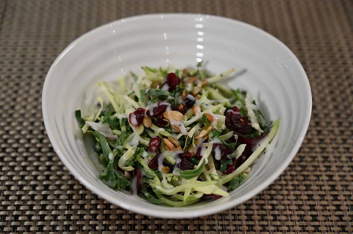 Costco Eat Smart Sweet Kale Salad Kit prepared with cranberries, pumpkin seeds and dressing in a white bowl. 