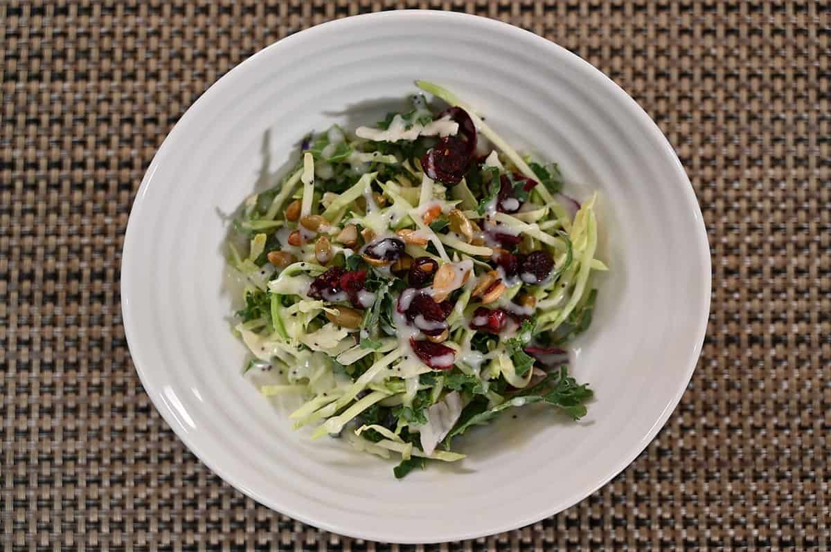 Costco Eat Smart Sweet Kale Salad Kit prepared with cranberries, pumpkin seeds and dressing in a white bowl. 