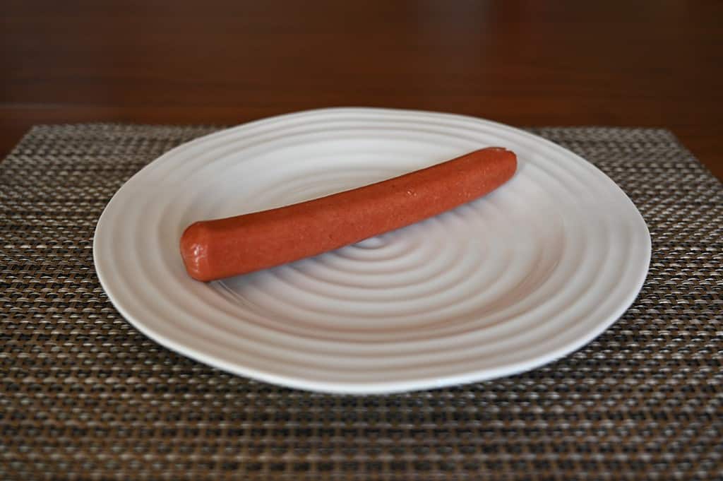 One Costco hot dog wiener on a white plate, uncooked. 