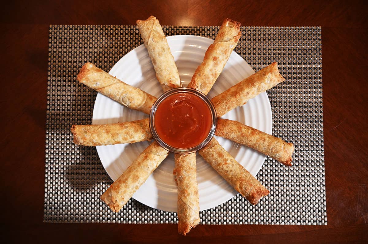 Image of the egg rolls cooked and served in a circular fashion on a white plate with a dipping sauce in the middle.