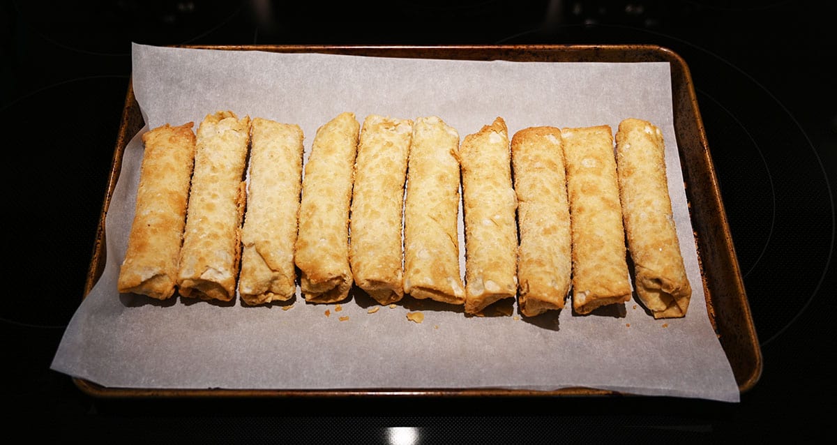 Egg rolls on a parchment lined baking tray being cooked in the oven.
