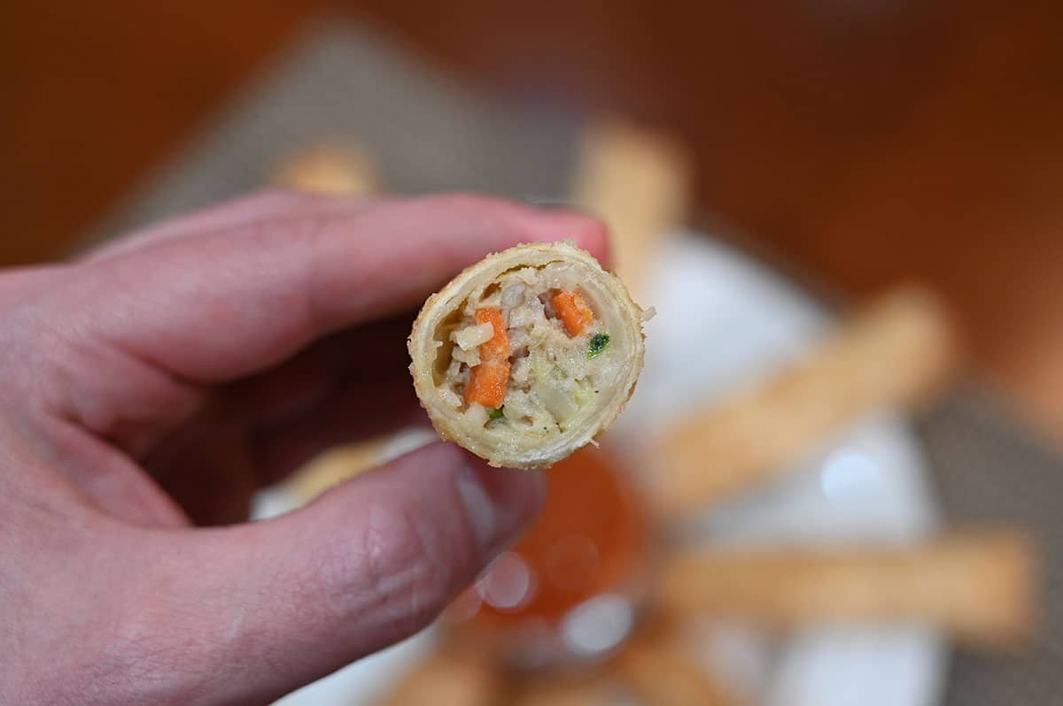 Closeup image of an egg roll being held up by a hand, the egg roll is cut in half so you can see the filling.