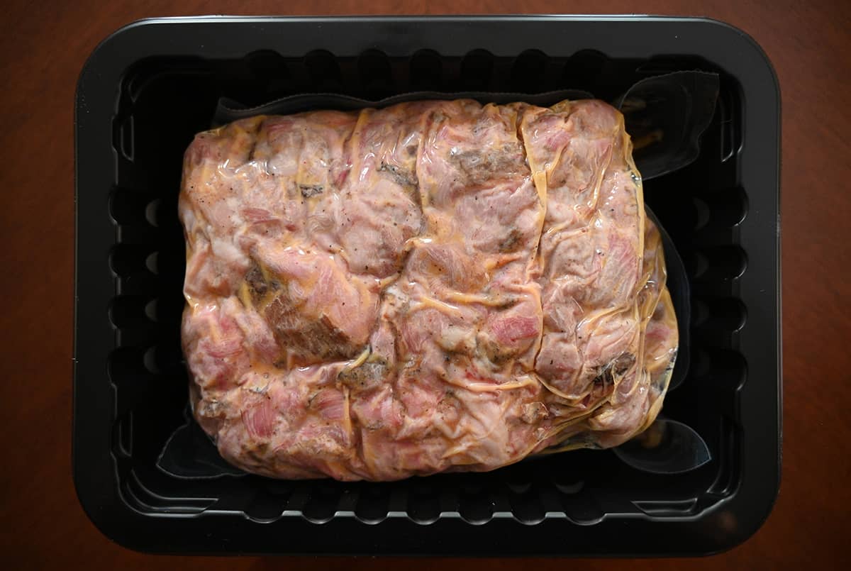 Top down image of the pulled pork sealed in a plastic bag sitting in a tray before cooking it in the microwave.