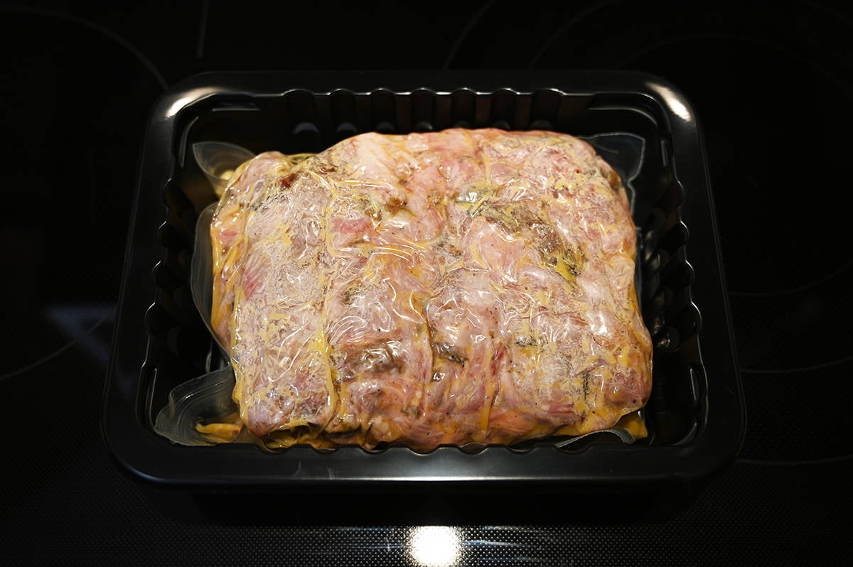 Top down image of the pulled pork sealed in a plastic bag sitting in a tray after heating it in the microwave.