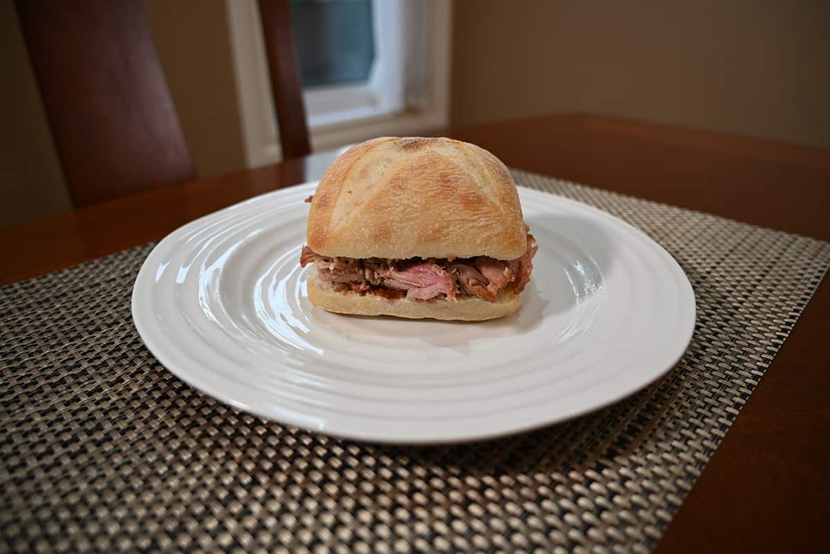 Side view image of a pulled pork sandwich served on a white plate.