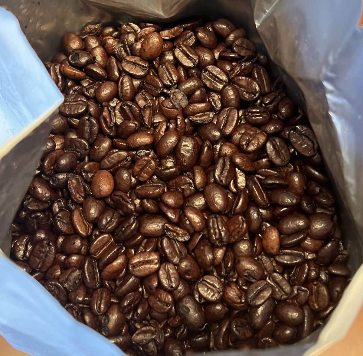 Top down image of the bag of whole coffee beans opened so you can see the beans. They appear dark and shiny.