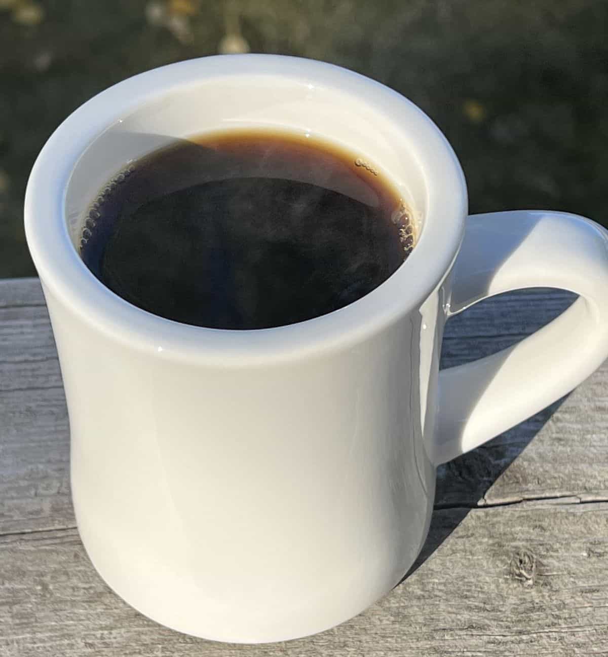 Image of one cup of black coffee sitting on a deck outside. 