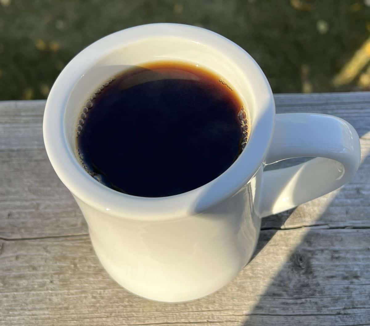 Top down image of one cup of coffee sitting outside on a ledge of a deck.