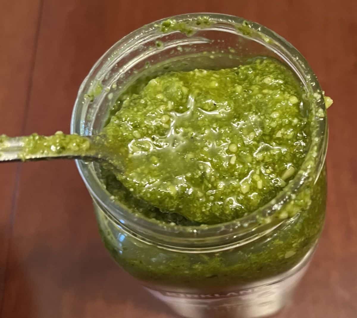 Image of a spoonful of basil pesto hovering over the container of pesto.