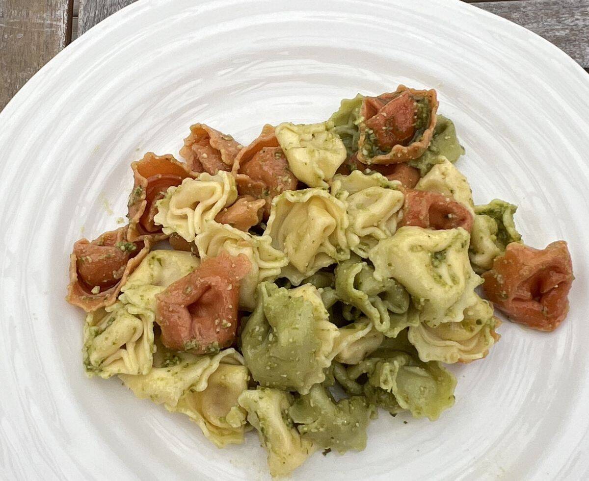 Top down image of a bowl of cooked tortellini with pesto sauce on it.
