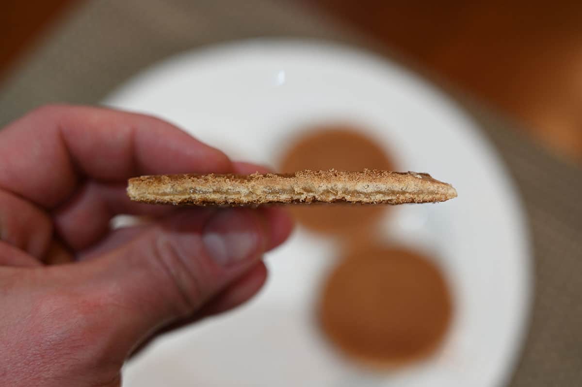 Side view image of a hand holding one stroopwafel cookie with a bite taken out of it so you can see the middle.