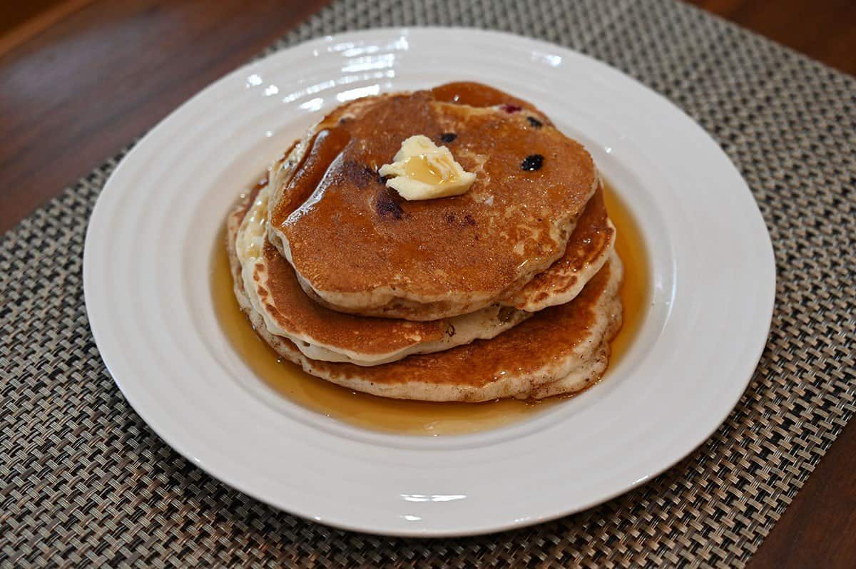 Image of Costco maple syrup poured over a large stack of pancakes on a white plate. 