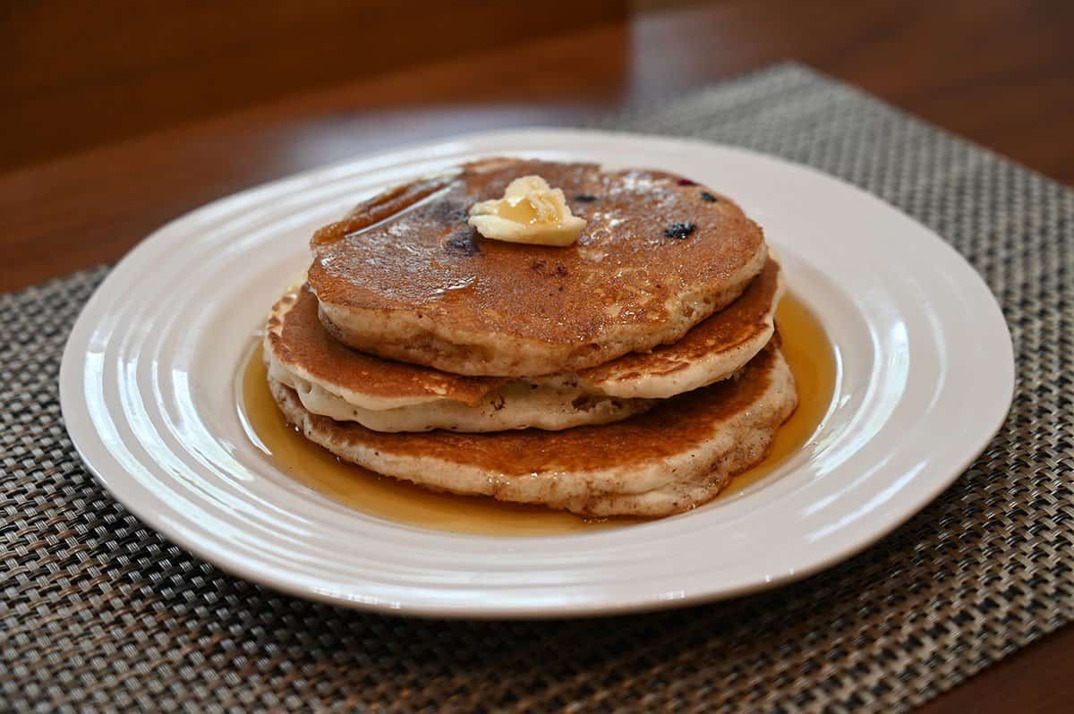 Image of Costco maple syrup poured over a large stack of pancakes on a white plate. 