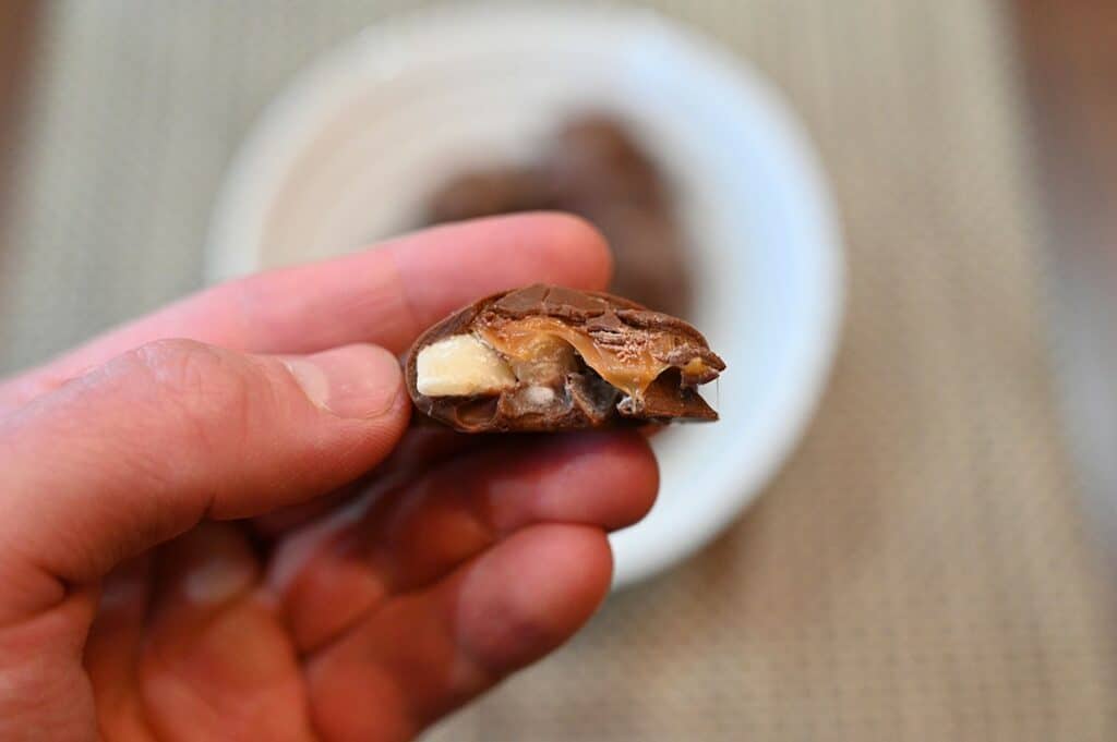 Closeup image of one of the Costco Kirkland Signature Macadamia Clusters with a bite taken out so you can see the macadamia inside and salted caramel. 