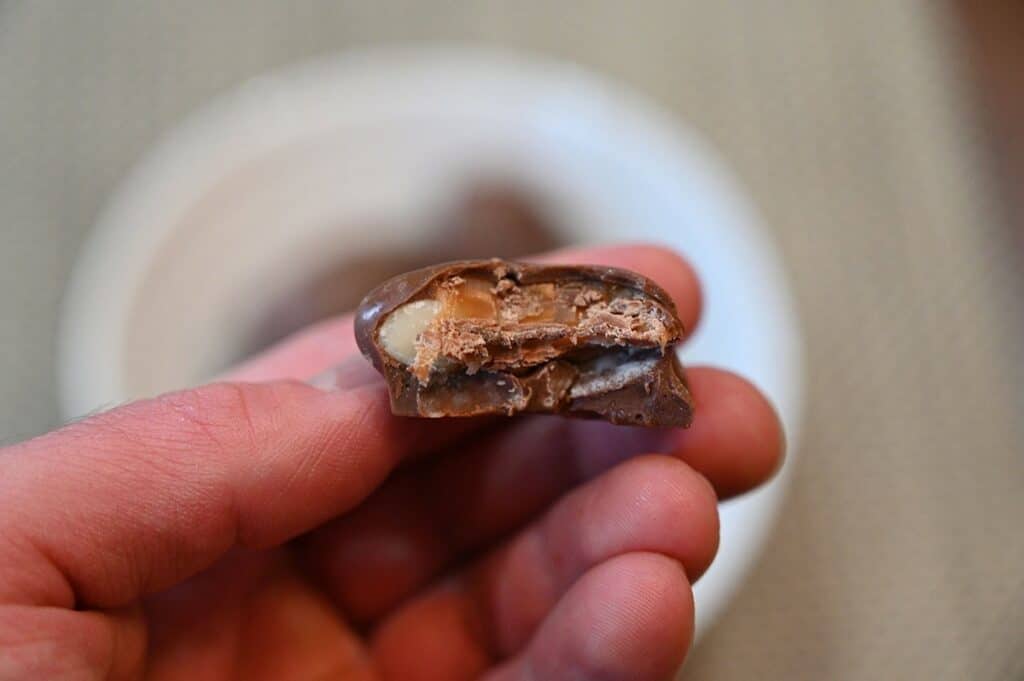 Closeup image of one of the Costco Kirkland Signature Macadamia Clusters with a bite taken out so you can see the macadamia inside and salted caramel. 