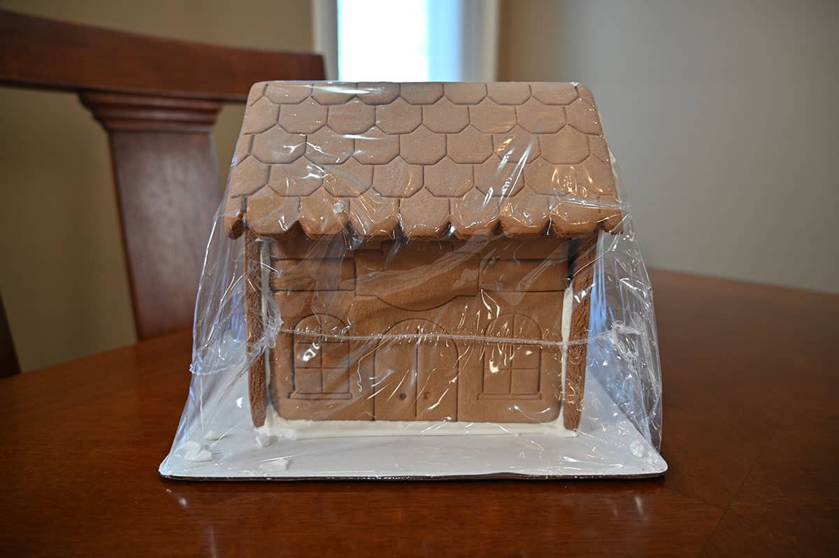 Image of the gingerbread mansion in the plastic wrap and sitting on a piece of cardboard, ready to decorate.