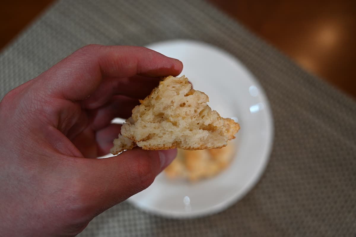 Image of hand holding one biscuit close to the camera with a bite taken out so you can see the inside.