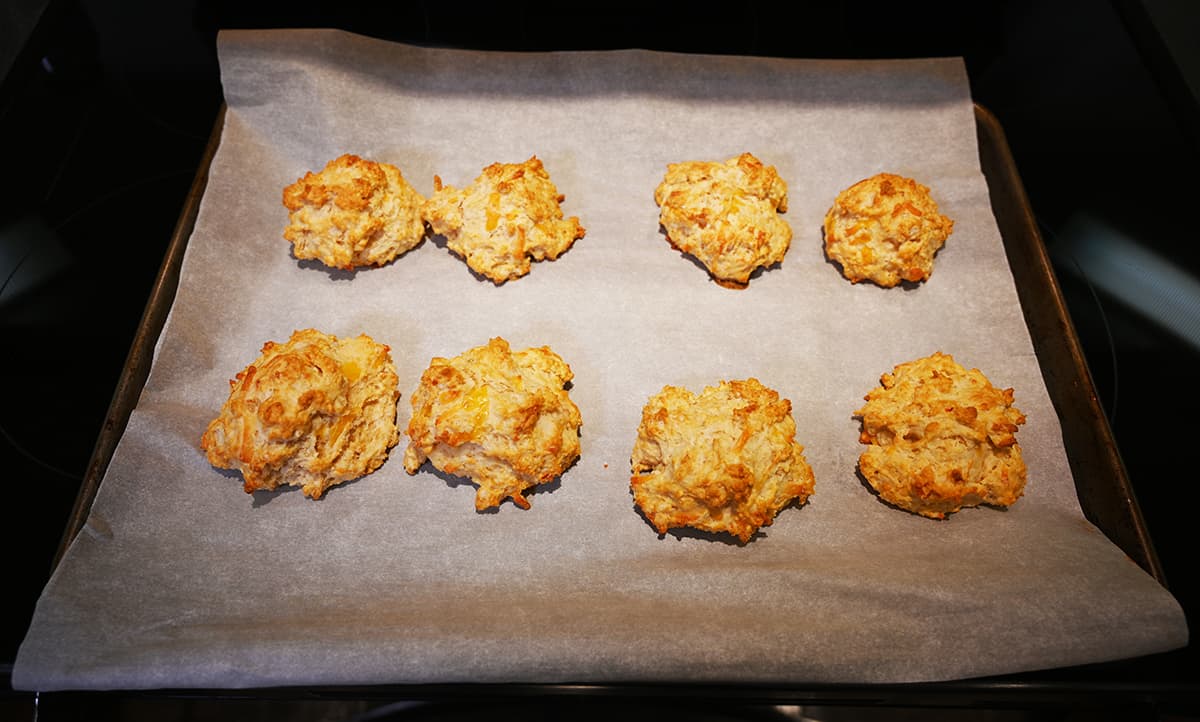 Image of a baking tray lined with parchment paper on the top of an oven with baked biscuits on top.