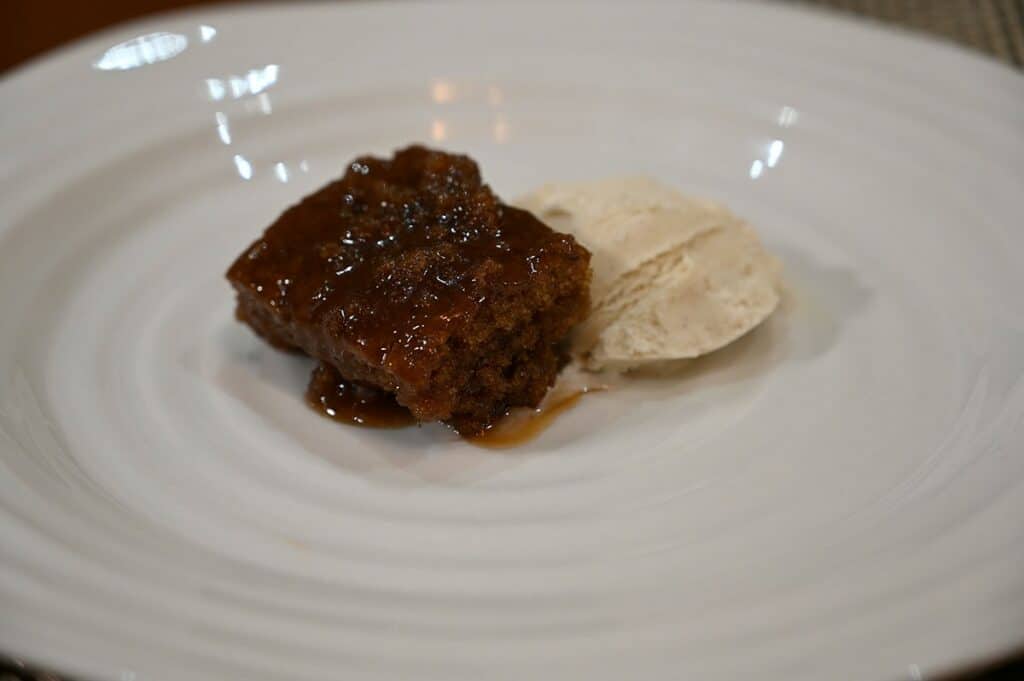 Image of a piece of the Costco The Sticky Toffee Pudding Co. Sticky Toffee Pudding plated with vanilla ice cream beside it. 