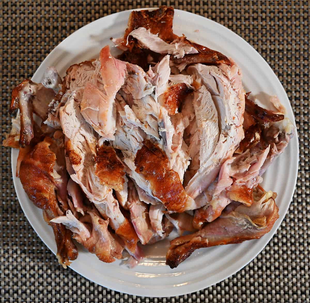Image of the rotisserie chicken all cut up and served on a white plate, top down image.