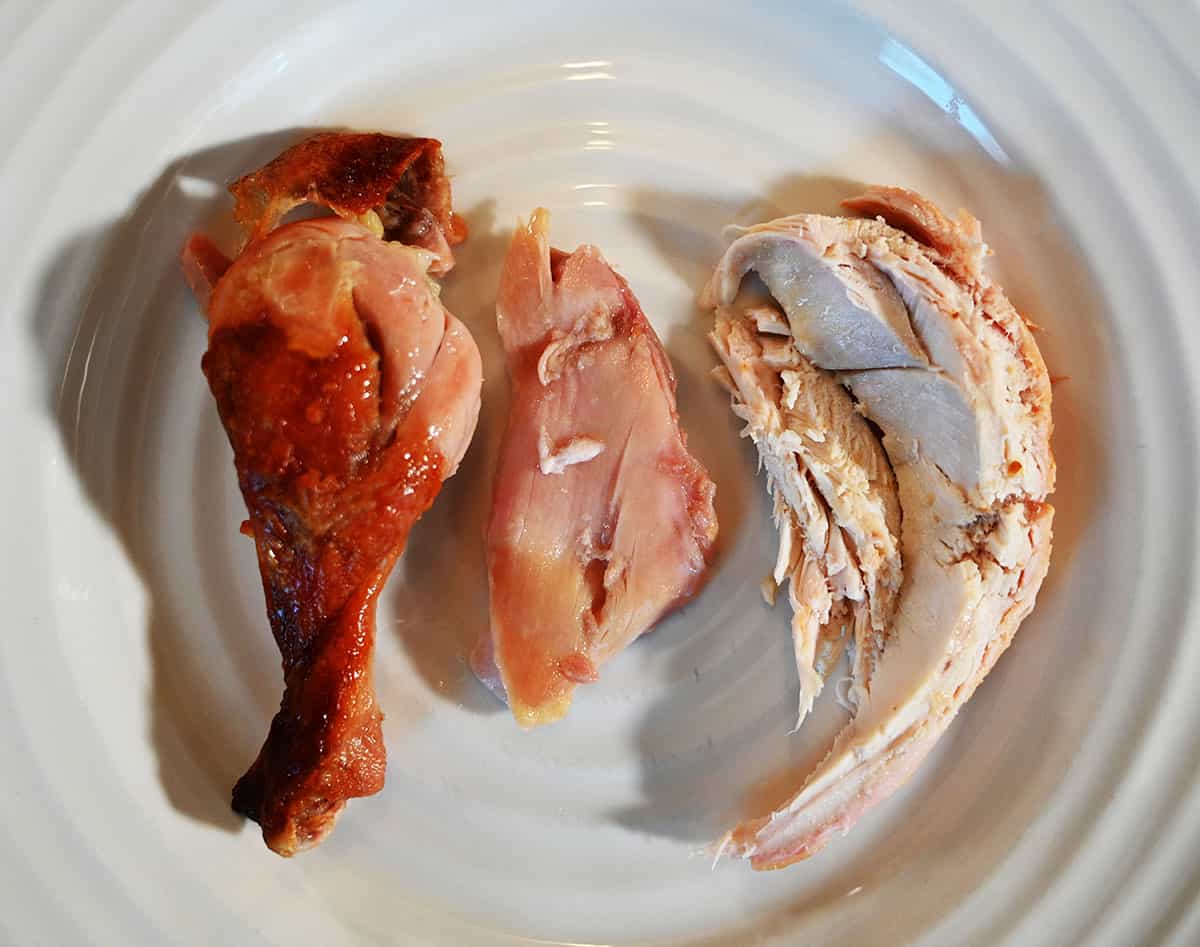 Image of a drumstick, dark meat and white meat from the rotisserie chicken served on a white plate.