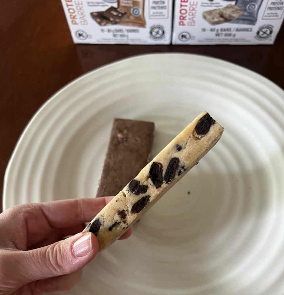 Image of a hand holding one cookies and cream Costco protein bar close to the camera. 