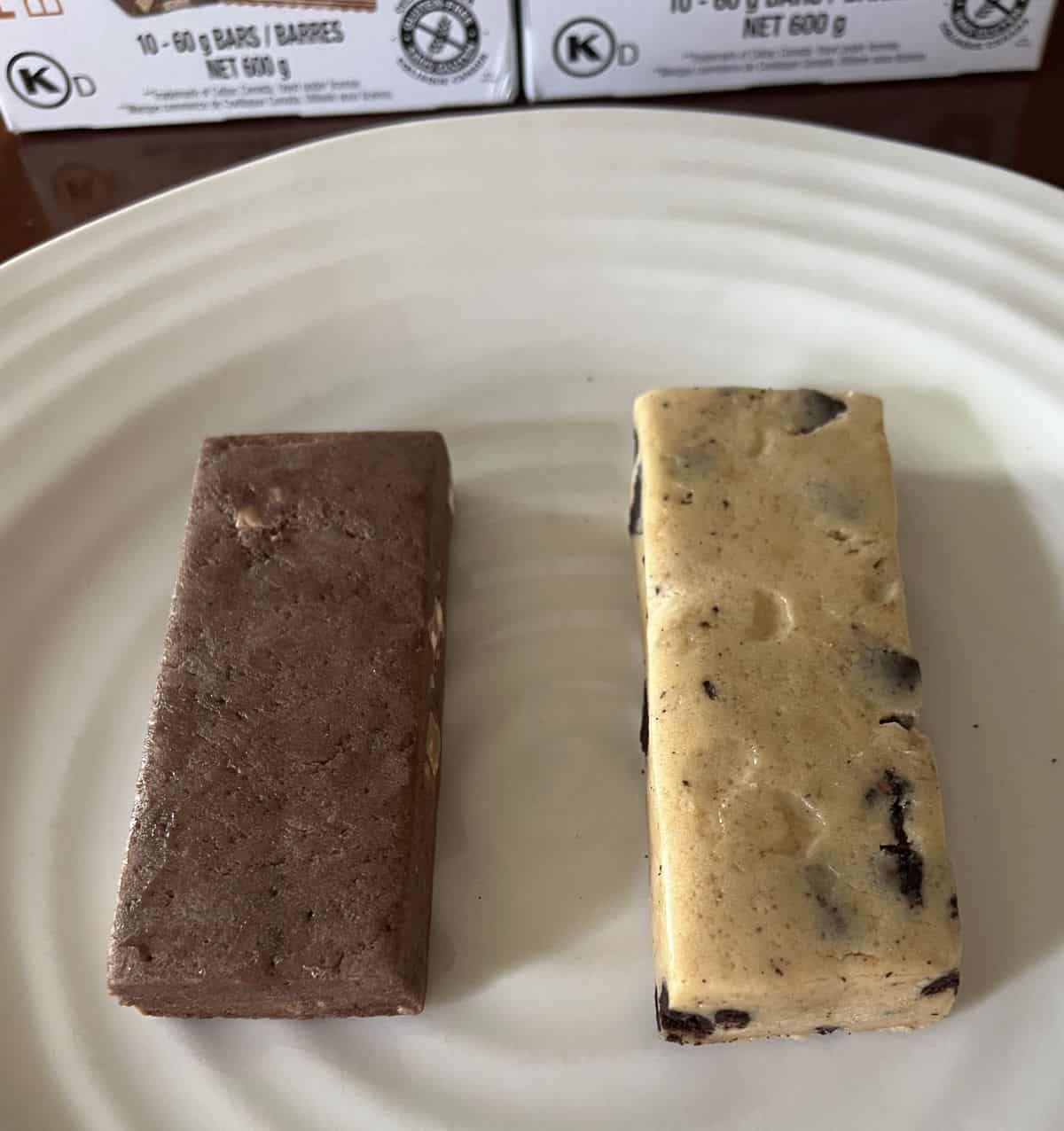 Image of one chocolate peanut butter and one cookies and cream protein bar served on a white plate.