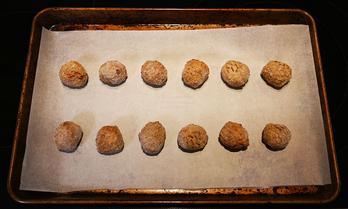 Image of a baking tray with parchment paper on it and frozen meatballs ready to be baked.