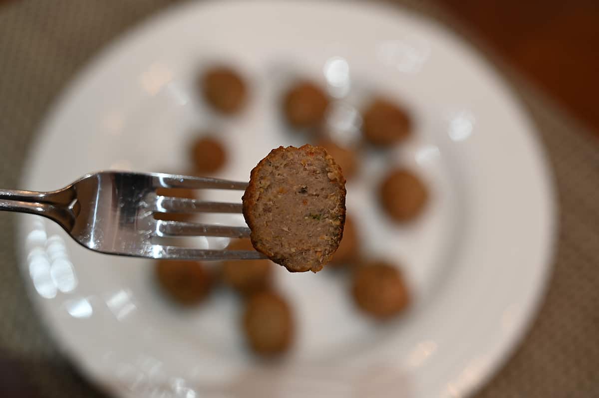 Closeup image of a meatball cut in half so you can see the center with a plate of meatballs in the background.