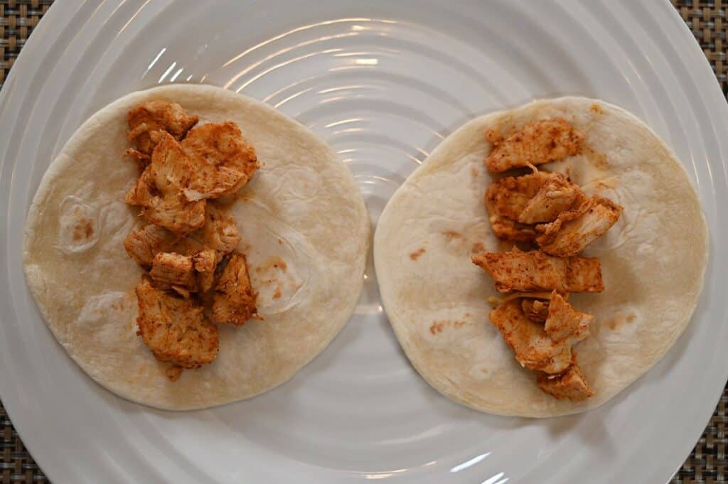 Two Costco Kirkland Signature Chicken Tacos prepared on a white plate with just chicken on top of two tortillas. 