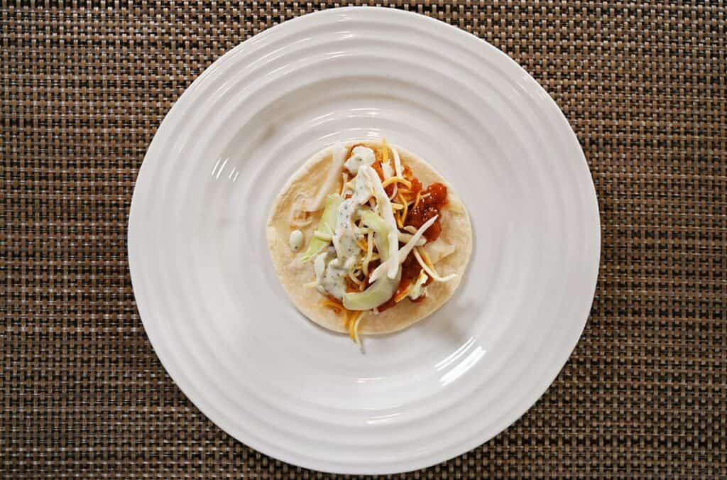 One Costco Kirkland Signature Chicken Taco fully loaded with all the ingredients and on a white plate. 