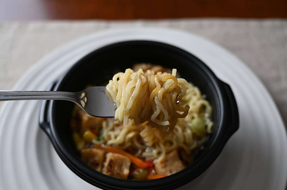 Closeup image of a fork with a bunch of noodles on it hovering over a bowl of ramen.