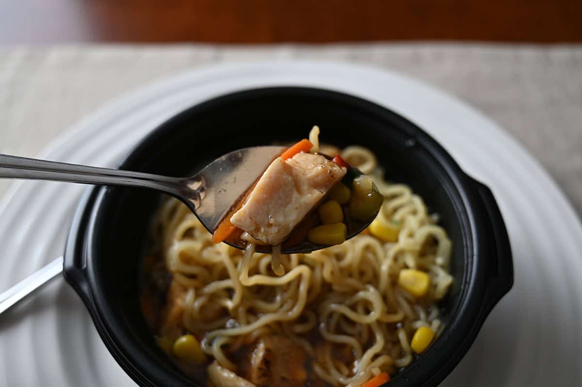 Closeup image of a spoon with chicken and corn on it hovering over a bowl of ramen.