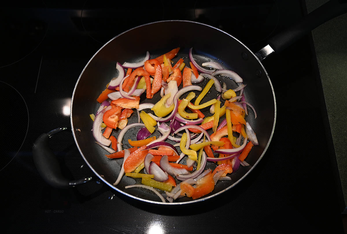 Top down image of bell pepper and onions being cooked in a pan.