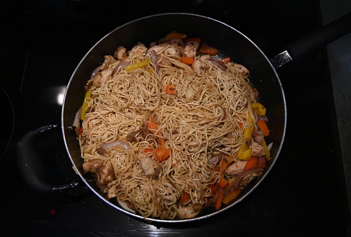 Top down image of the chicken chow mein in a big fry pan being mixed together to cook.