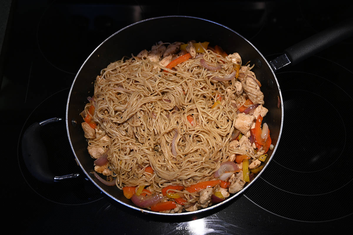 Top down image of the chicken chow mein in a big fry pan on a stovetop being cooked.