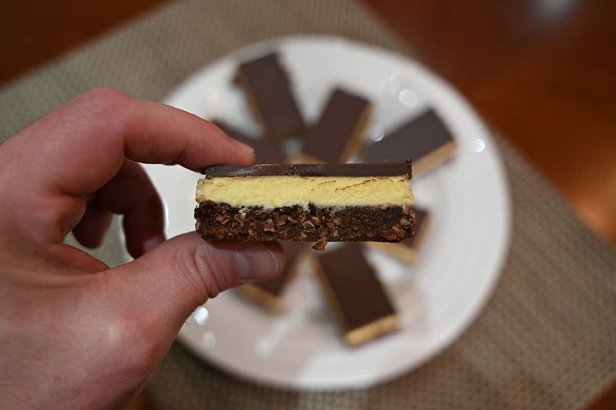 Close up image of a hand holding one Nanaimo bar so you can see each layer.