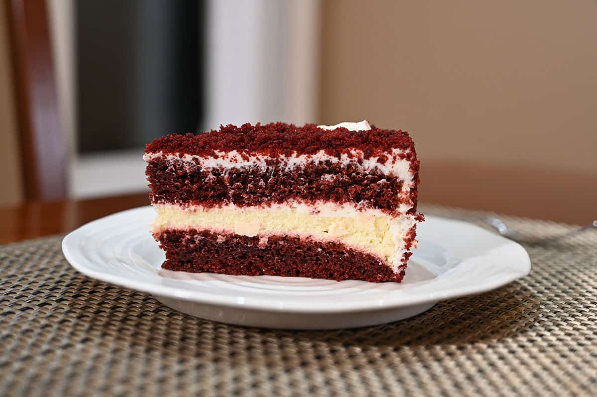 Side view image of one slice of red velvet cheesecake on a white plate.