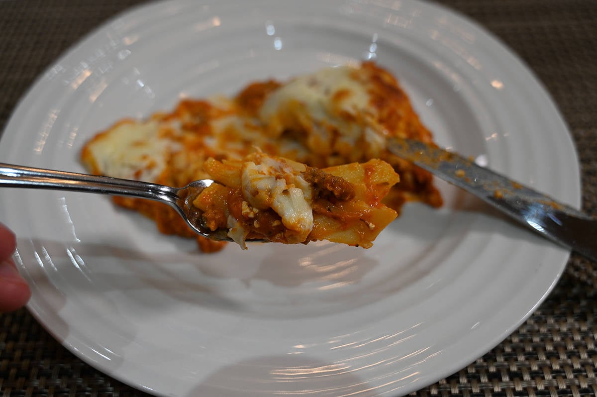 Closeup image of a fork with lasagna on it close to the camera so you can see the different layers. In the background is the plate of lasagna.