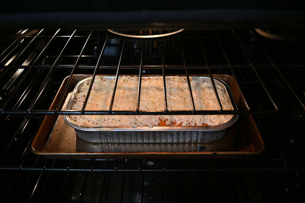 Image of a uncooked lasagna sitting on a baking tray inside an oven.