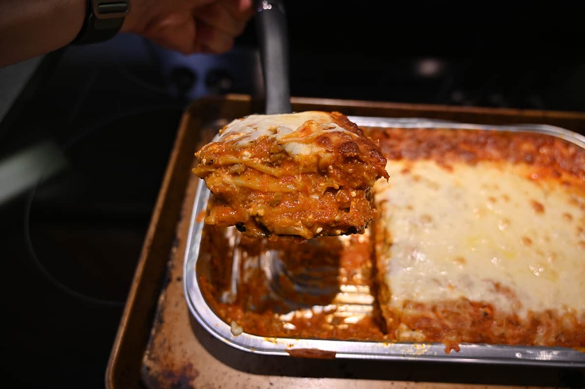 Side view image of a slice of lasagna being lifted out of the tray of lasagna on a spatula.