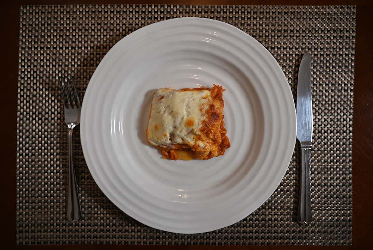 Top down image of a small piece of lasagna served on a white plate. The cheese on the top is very noticeable.