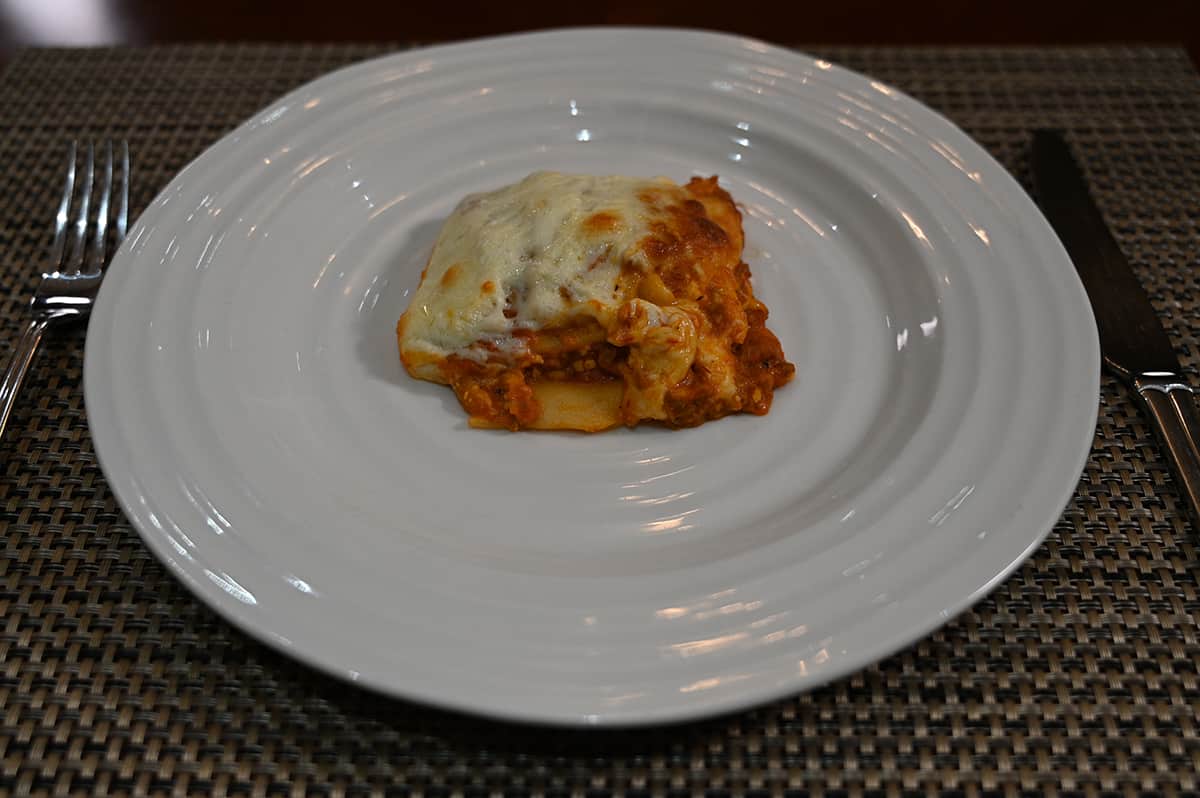 Side view image of a piece of lasagna on a white plate. Beside the plate is a fork.