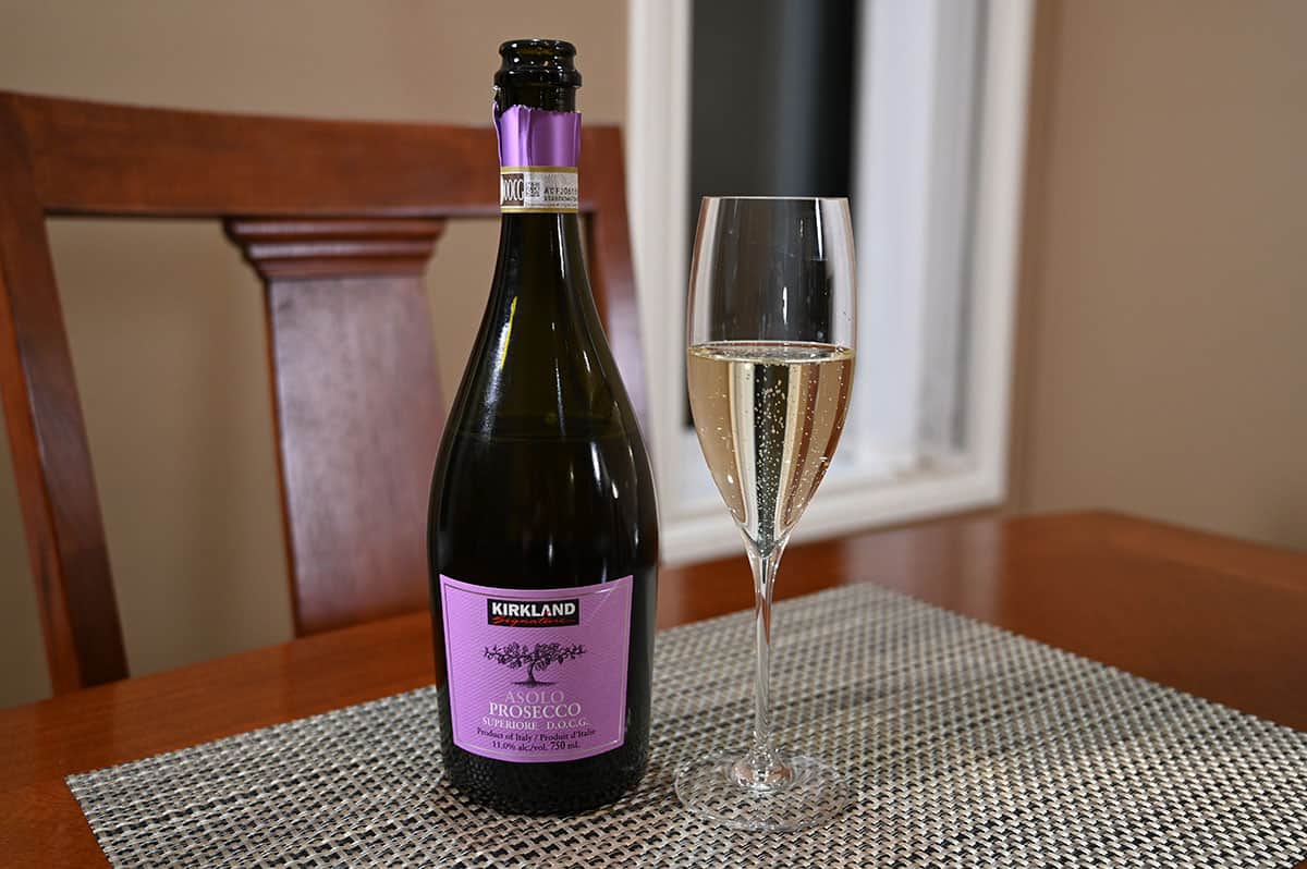 Image of the bottle of prosecco sitting on a table beside a poured glass of prosecco. 