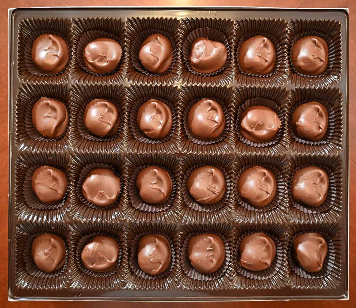 Image of the box of chocolate covered macadamia nuts with the lid off so you can see all the chocolates laying in the box.